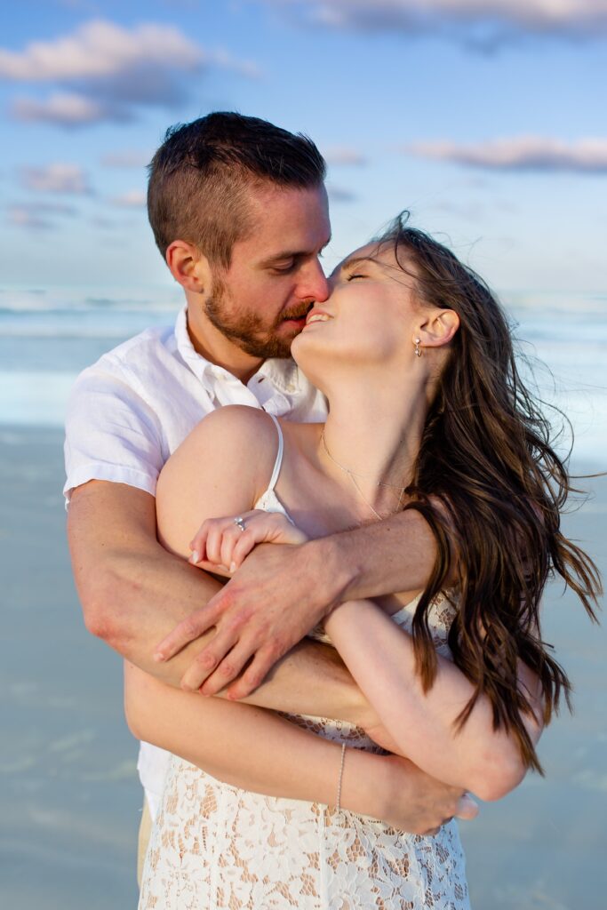 New Smyrna Beach Engagement Photo — Couple with arms wrapped around each other kissing on the beach at sunset