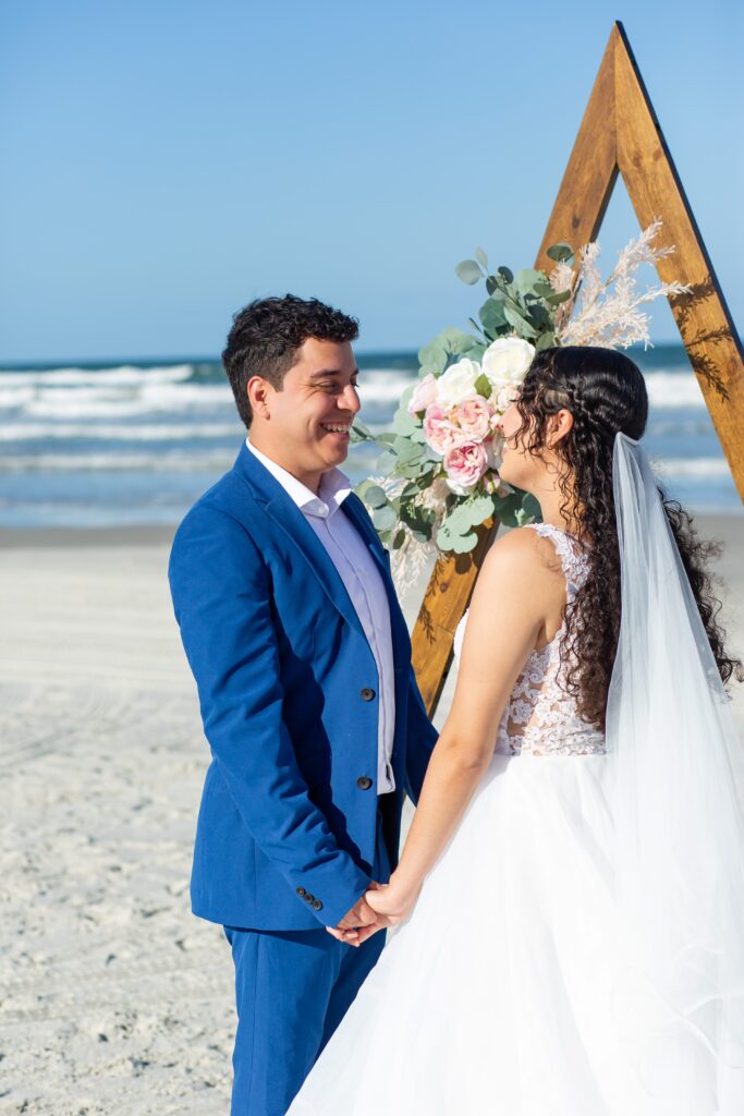 Groom in blue suit saying vows under triangle arch for his Florida Beach Wedding