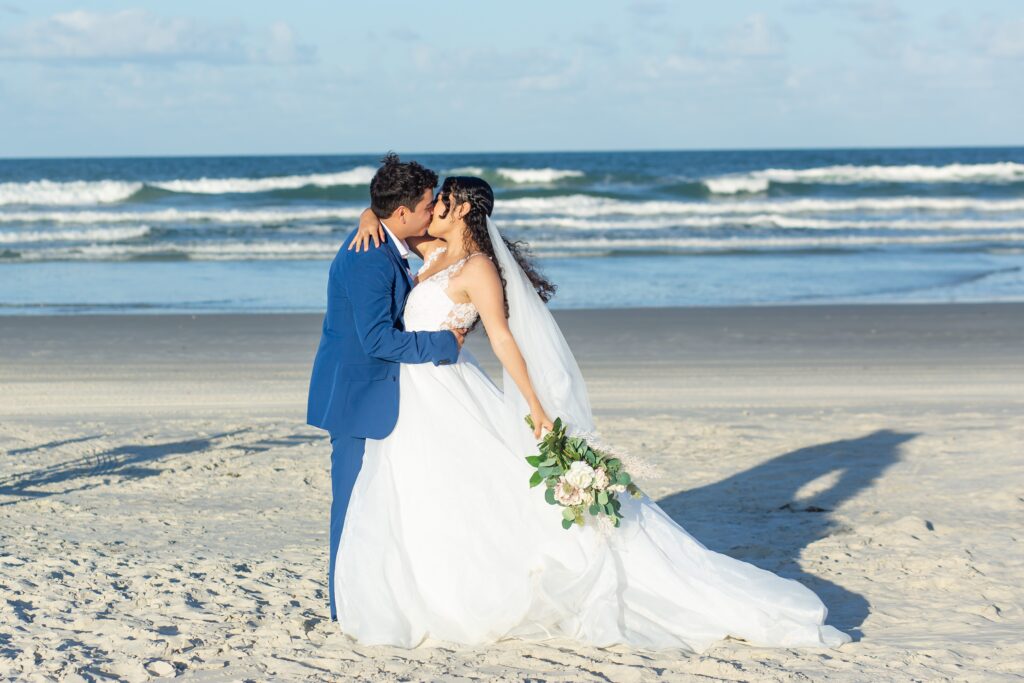 Bride with full gown veil and blush and cream bridal bouquet kissing on the beach after their Florida beach wedding