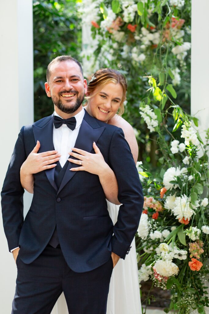 Bride holding on to Groom in navy suit under trellis after their elopement at Leu Gardens in Orlando