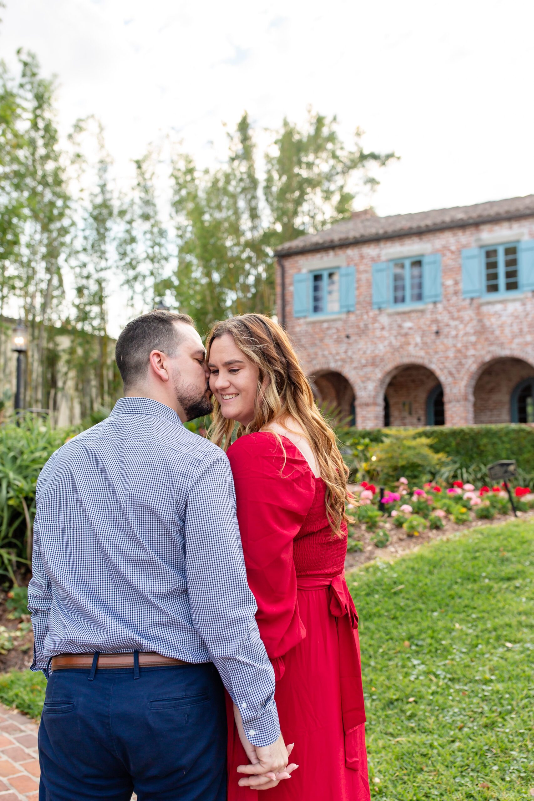 Casa Feliz Historic Home Orlando Engagement Photos — Guy kissing girl in front of spring flowers and brick arches at Spanish historic home in Winter Park, Florida