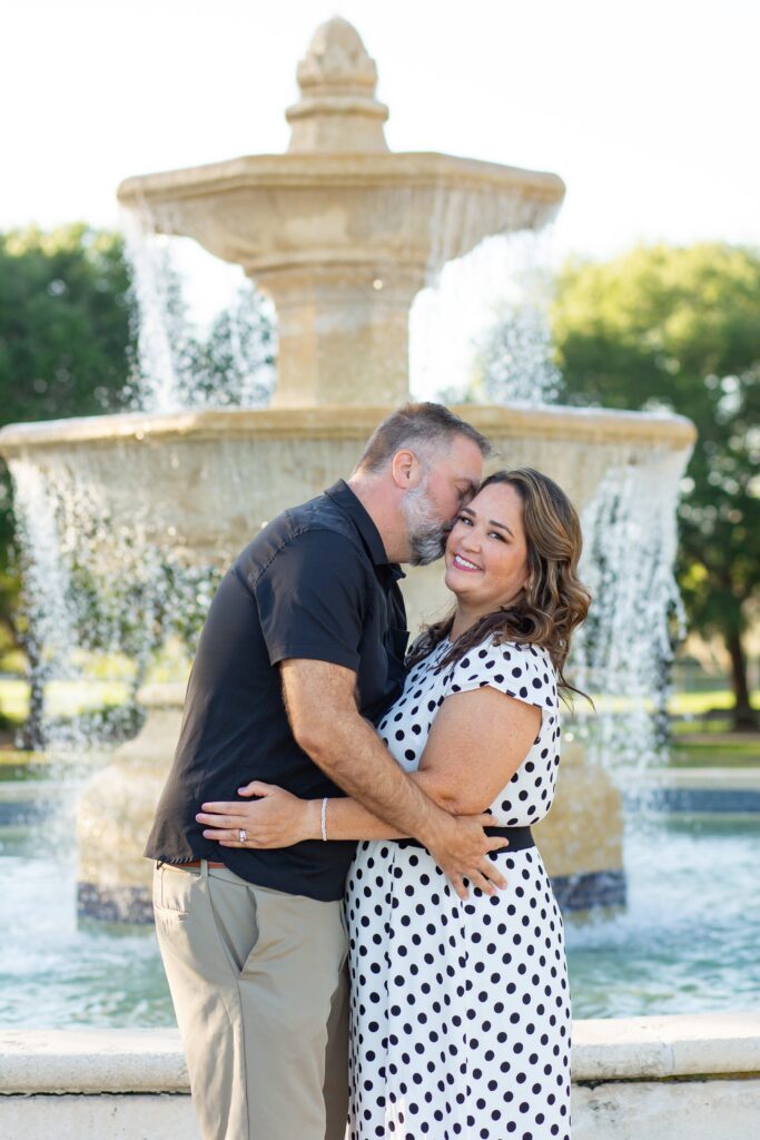Guy kissing girl's cheek in front of large fountain at Blue Jacket Park for their Orlando Date Night