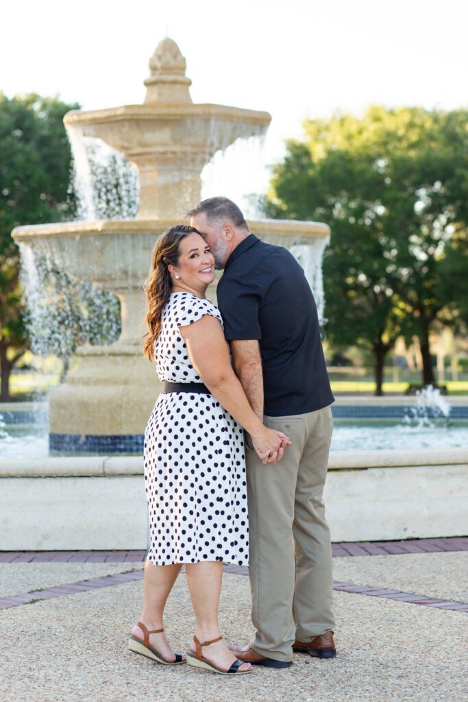 Guy kissing girl's cheek in front of large fountain at Blue Jacket Park in Orlando for their anniversary photo session