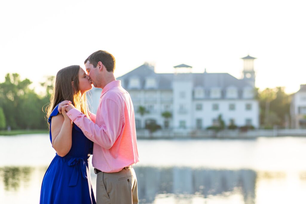 Couple holding hands and kissing in front of Bohemian Hotel in Celebration Florida Orlando overlooking the water at sunset for their engagement photos