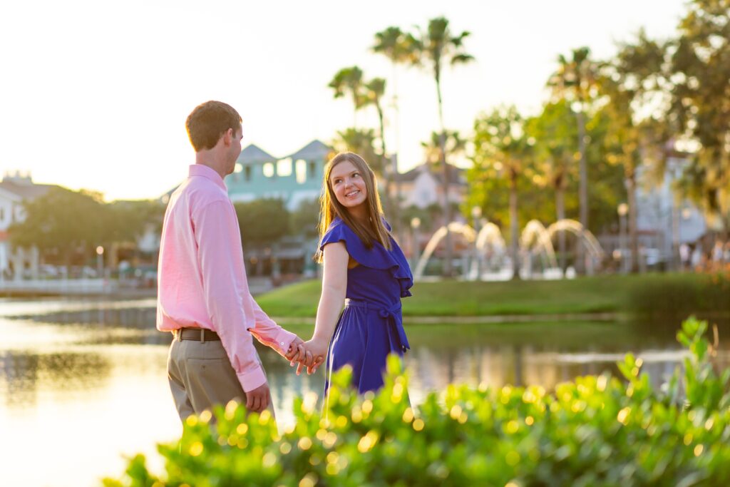 Couple holding hands in front of palm trees in Celebration Florida Orlando overlooking the water at sunset for their engagement photos