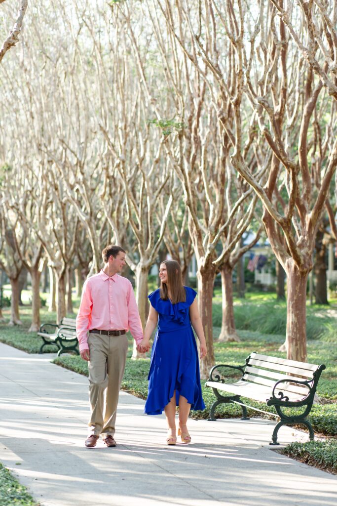 Couple holding hands and walking in front of trees in Celebration Florida Orlando for their engagement photos