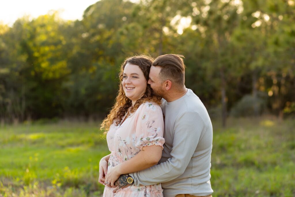 Guy in gray shirt wraps arms around girl wearing light pink maxi dress in field for their engagement photos at Lake Louisa State Park in Orlando