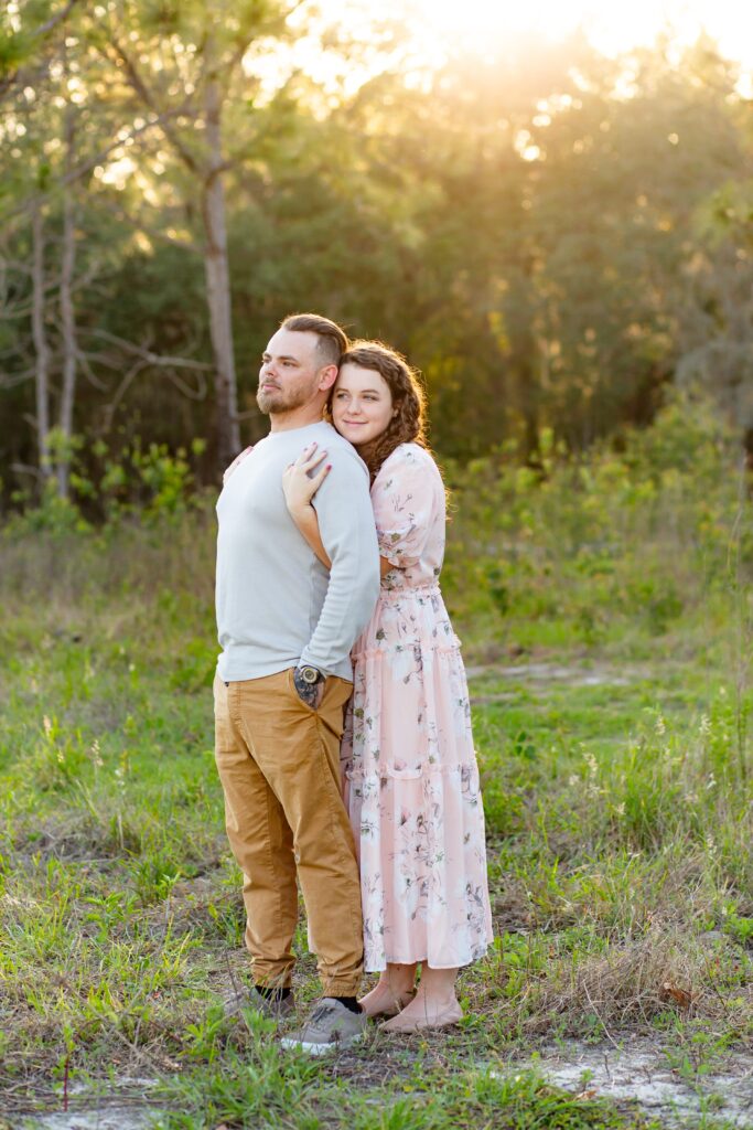 Girl wearing light pink maxi dress wraps arms around Guy in gray shirt in field at sunset for their engagement photos at Lake Louisa State Park in Orlando