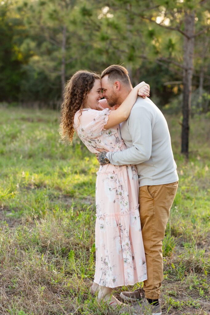 Guy in gray shirt wraps arms around girl wearing light pink maxi dress in field for their engagement photos at Lake Louisa State Park in Orlando