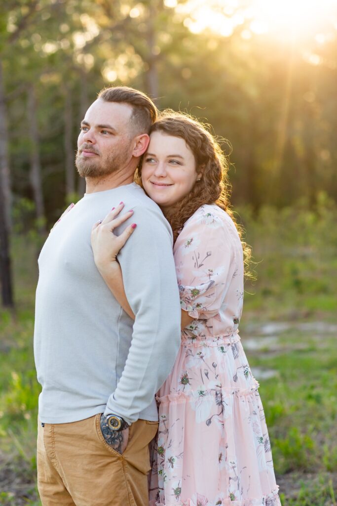 Girl wearing light pink maxi dress wraps arms around Guy in gray shirt in field at sunset for their engagement photos at Lake Louisa State Park in Orlando
