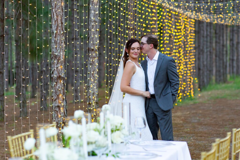 Bride and Groom standing in front of White and Green reception table with gold chairs and magical twinkle lights at Forest Wedding Venue in Florida