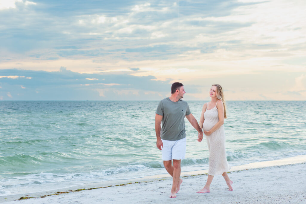 Couple walking on the beach at sunset for their Anna Maria Island maternity session