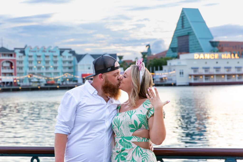 Couple celebrating and kissing after their Disney Proposal at the Boardwalk in front of the water