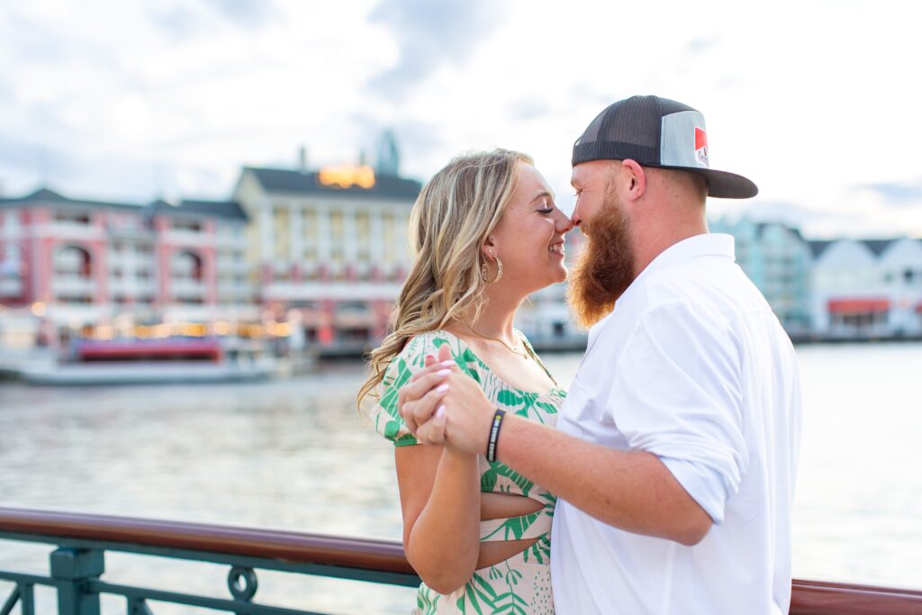 Couple holds hands as they stand in front of the water at the Boardwalk for their Disney Engagement Photos