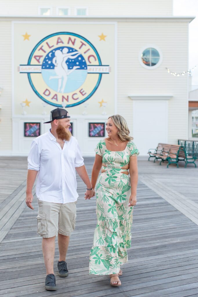 Couple walking and holding hands in front of the Dance Hall at the Boardwalk for their Disney Engagement Photos