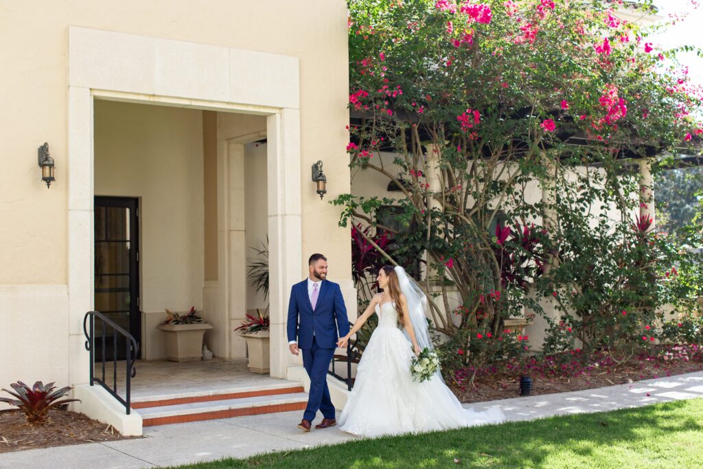 Bride and Groom walk in front of beautiful pink flower and ivy wall on their wedding day at the Alfond Inn in Winter Park, Florida