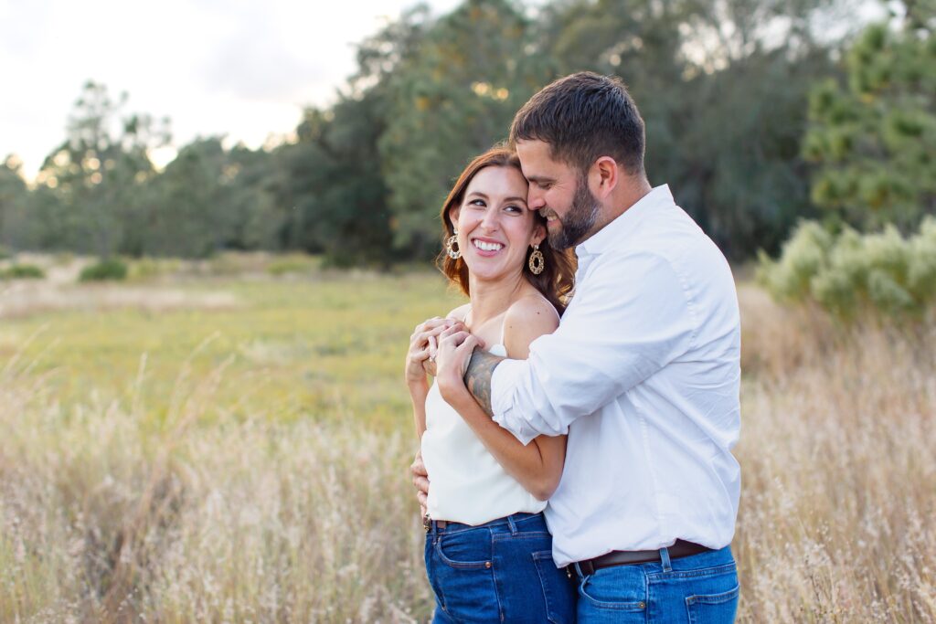 Guy hugs girl in field for their engagement photos at Lake Louisa State Park in Orlando Florida