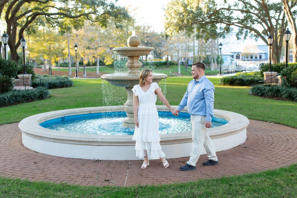 Couple holds hands and walks in front of fountain for their Disney Engagement Photos at Port Orleans Resort