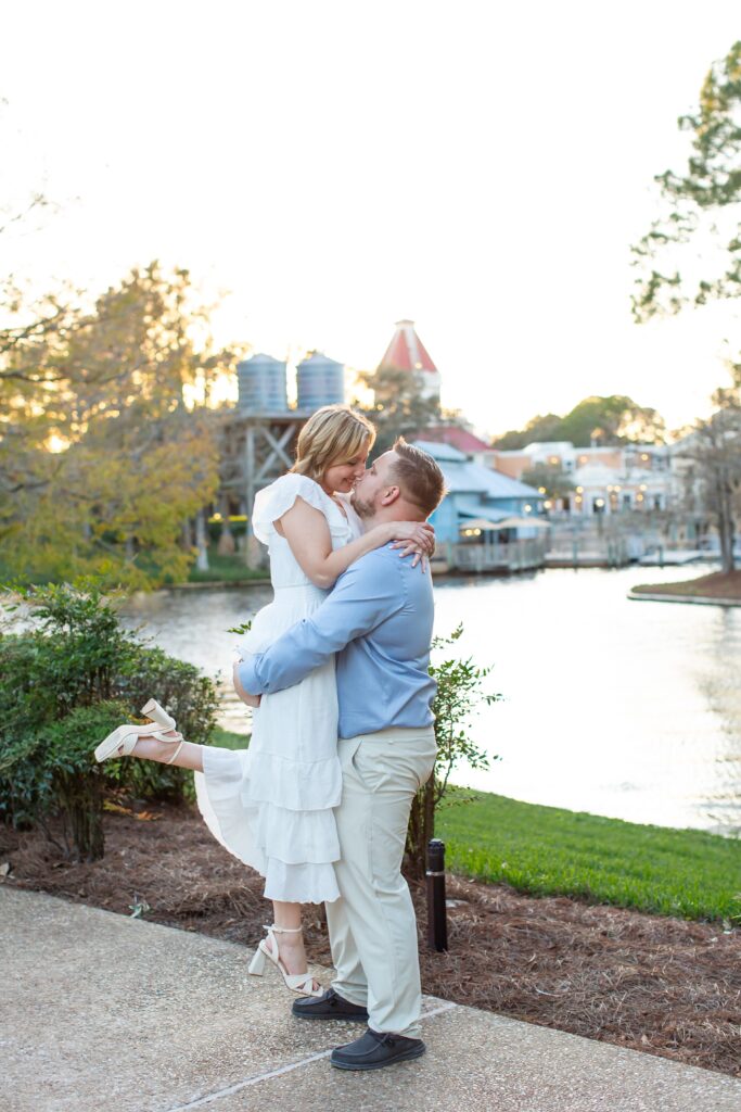 Guy lifts girl and kisses her in front of Riverside scene at sunset for their Disney Engagement Photos at Port Orleans Resort