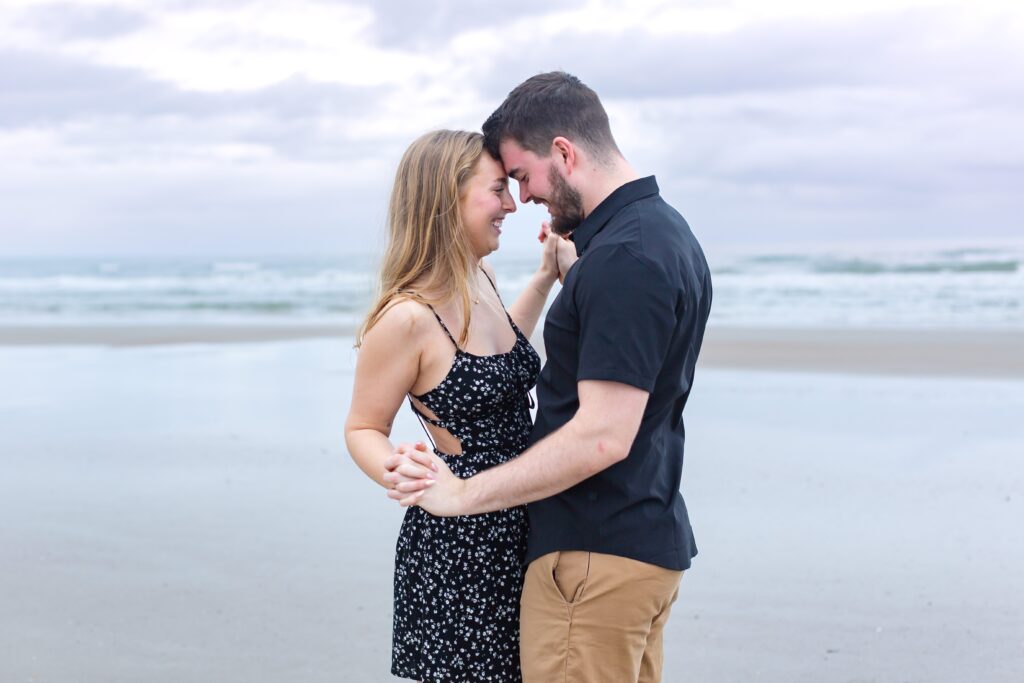 Couple holds hands and snuggles close to each other for their New Smyrna Beach photos 