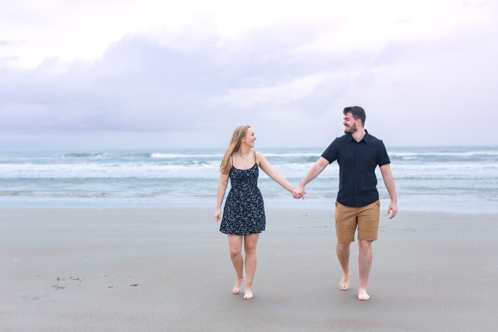 Couple holds hands and walks on beach after their proposal for their New Smyrna Beach Photos