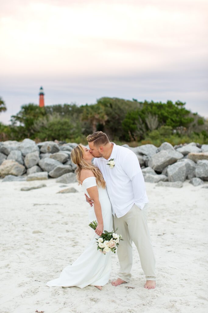 Couple kissing on the beach in front of lighthouse at their Florida Beach Wedding at Ponce Inlet Beach, Florida