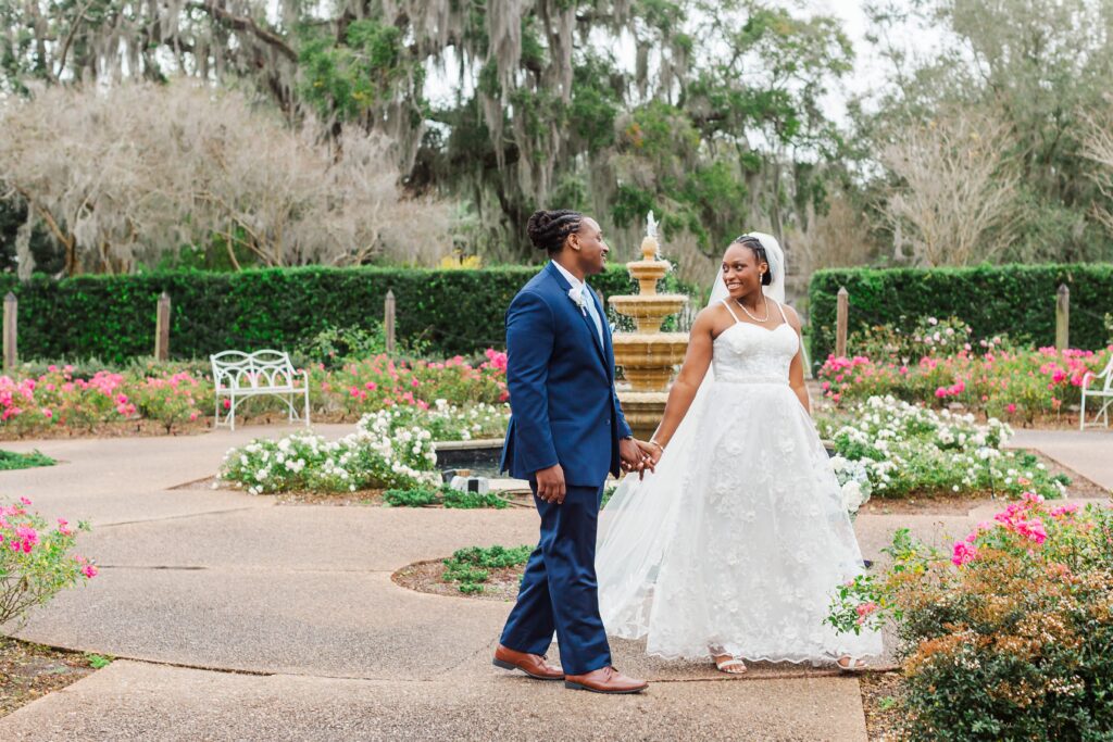 Bride and Groom walk in blooming rose garden with fountain behind them after their elopement at Leu Gardens in Orlando, Florida