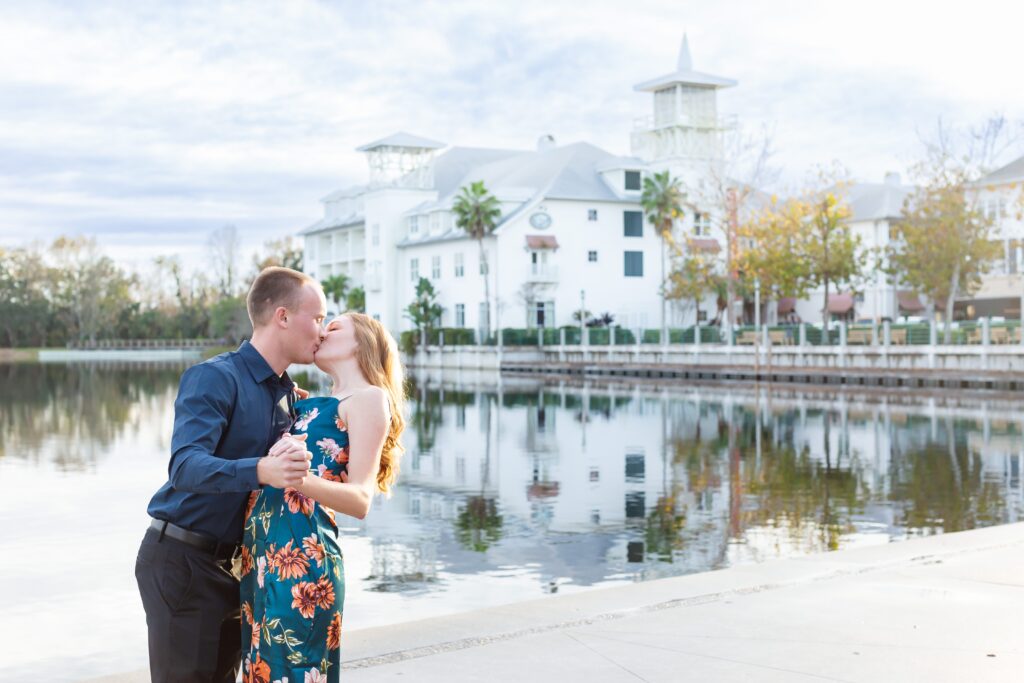 Couple kisses by the water in front of the Celebration Bohemian Hotel for their engagement photos in Celebration, Florida