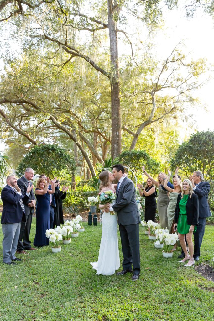 Bride and Groom kiss after their wedding ceremony while family and friends cheer them on at their back yard wedding in Orlando, Florida