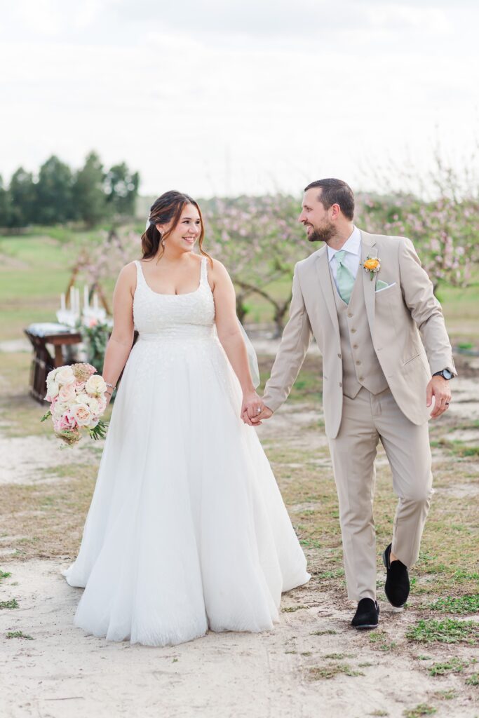 Bride and Groom walking through peach blossoms after their wedding at Acres of Grace Wedding Venue in Central Florida