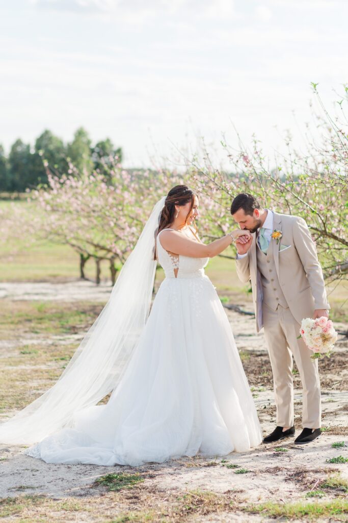 Groom kisses Bride's cheek standing in the peach blossoms after their wedding at Acres of Grace Wedding Venue in Central Florida