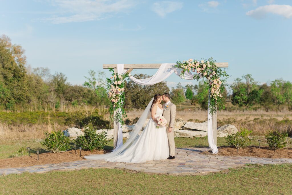 Bride and Groom stand under wedding ceremony arch at Acres of Grace Wedding Venue in Central Florida