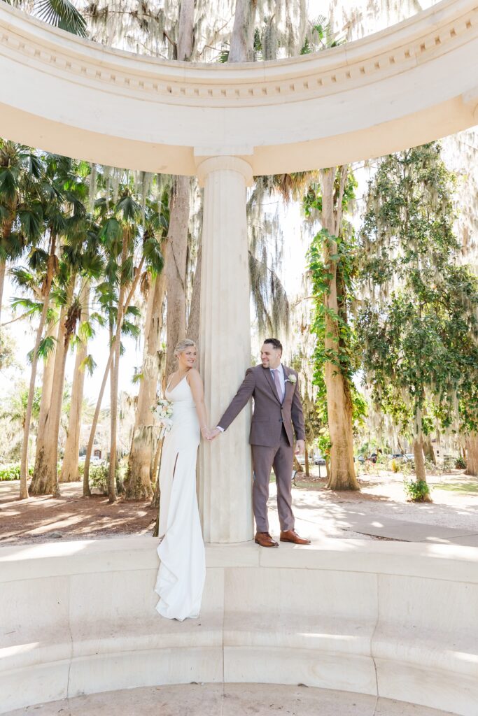 Bride and Groom hold hands at the exedra columns at Kraft Azalea Garden Wedding in Orlando, Florida