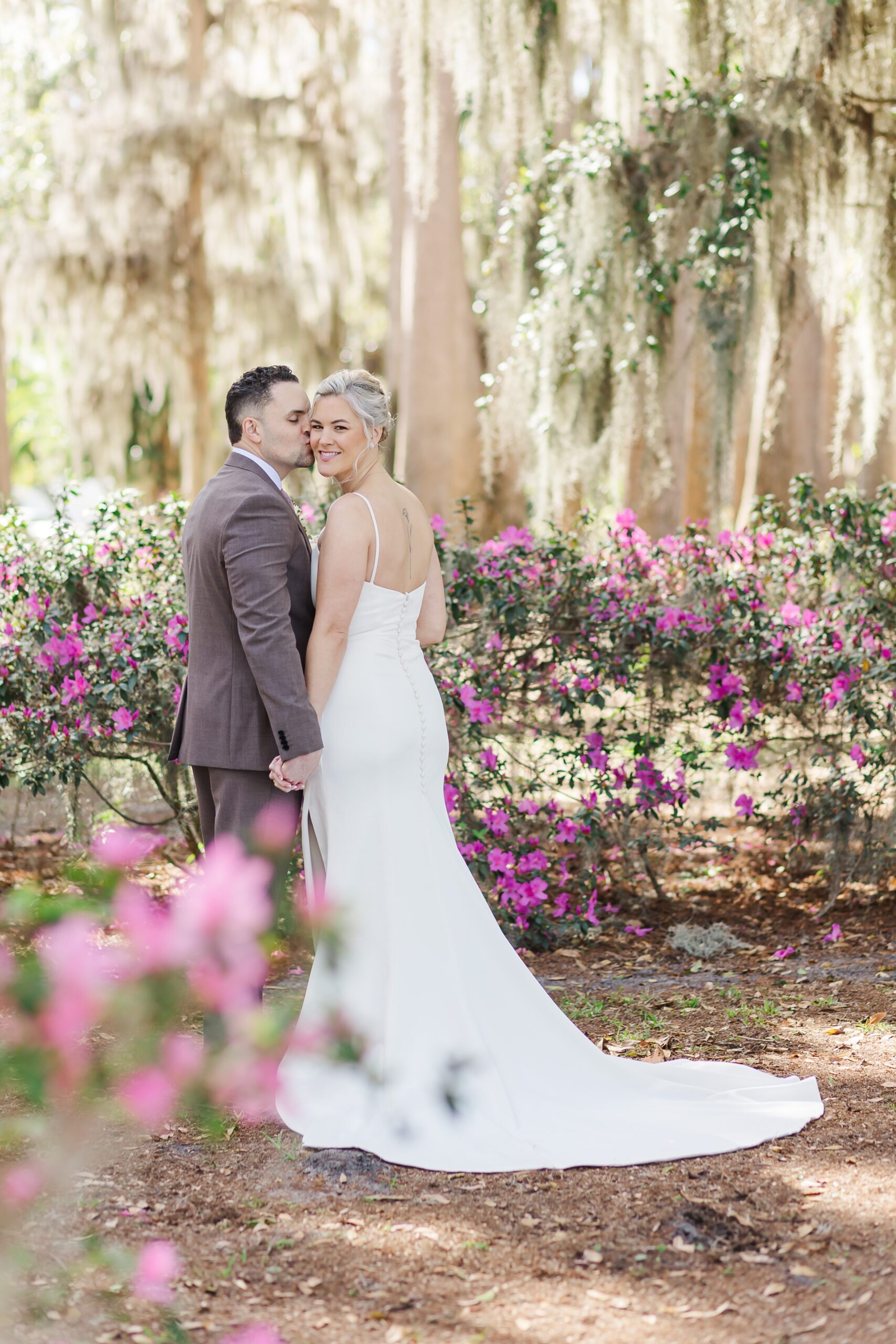 Groom kisses Bride's cheek by purple azaleas under beautiful live oak trees and moss at Kraft Azalea Garden Wedding in Orlando, Florida