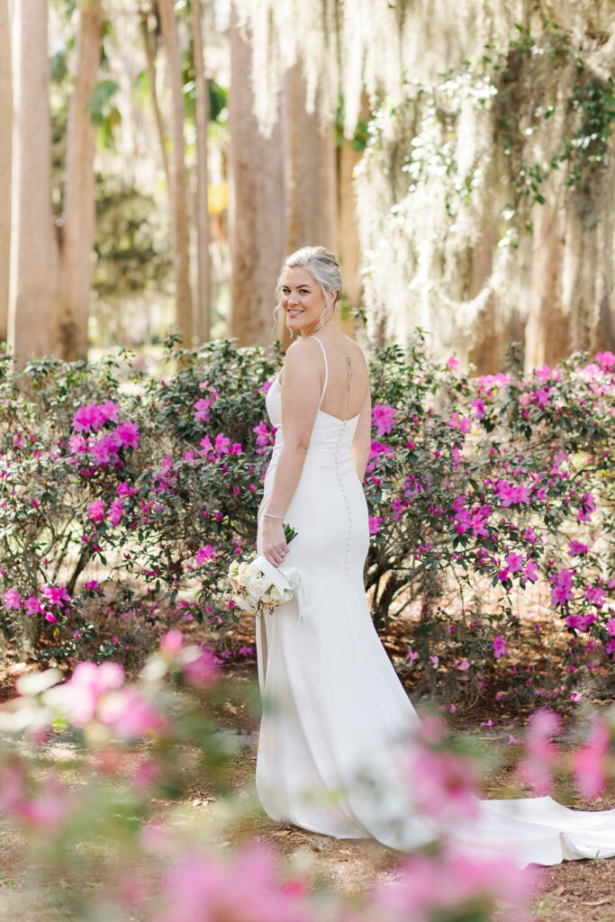Bride stands by purple azaleas under beautiful live oak trees and moss at Kraft Azalea Garden Wedding in Orlando, Florida
