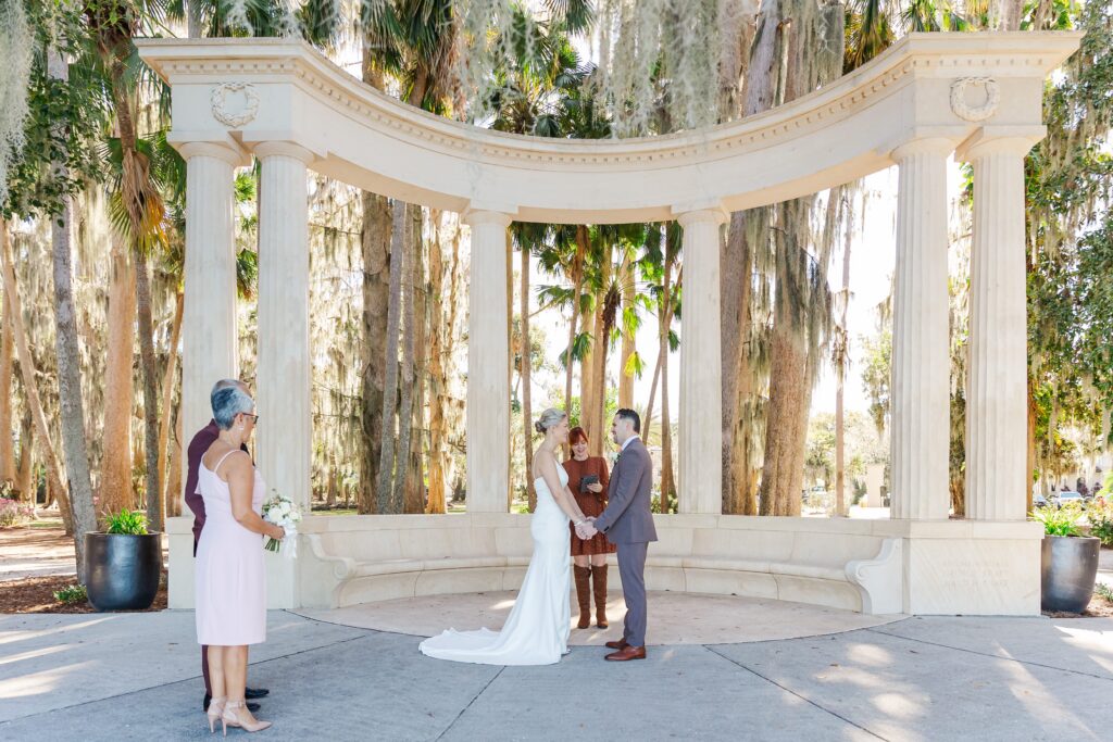 Bride and Groom hold hands at the exedra columns for their wedding ceremony at Kraft Azalea Garden Wedding in Orlando, Florida