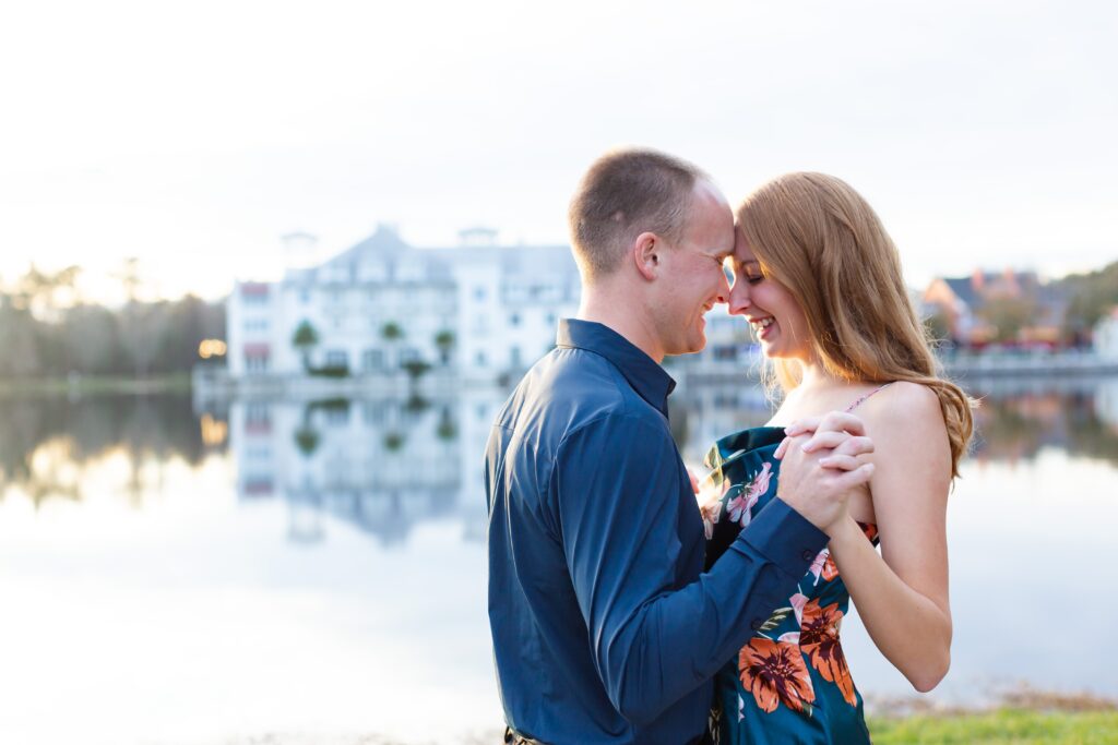 Couple holds hands and snuggles by the water in front of the Celebration Bohemian Hotel for their engagement photos at sunset in Celebration, Florida