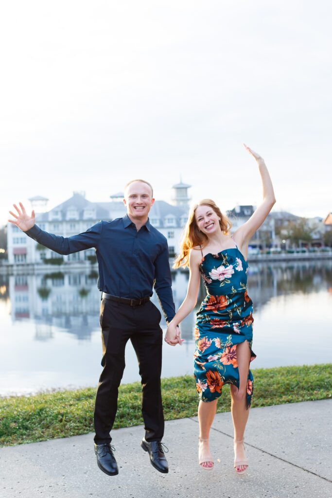 Couple jumping to celebrate their proposal by the water in front of the Celebration Bohemian Hotel at sunset in Celebration, Florida