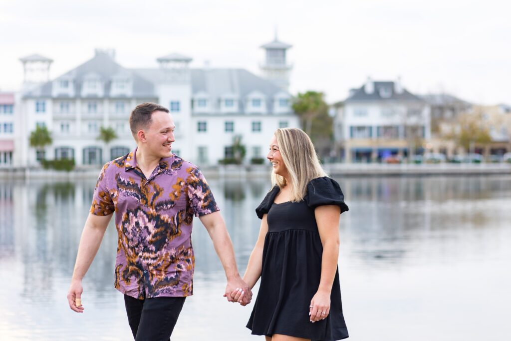 Couple walks holding hands and smiling together for their engagement photos in front of the Bohemian Hotel in Celebration, Florida