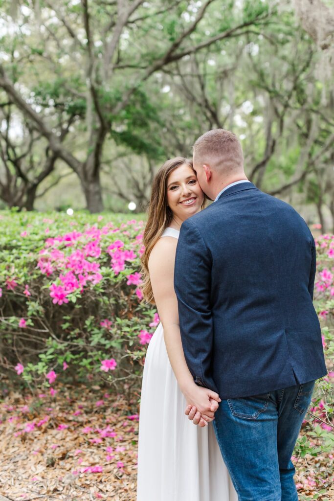 Guys kisses girl's cheek in front of pink flowers for their Orlando Engagement Photos at Cypress Grove Park in Orlando
