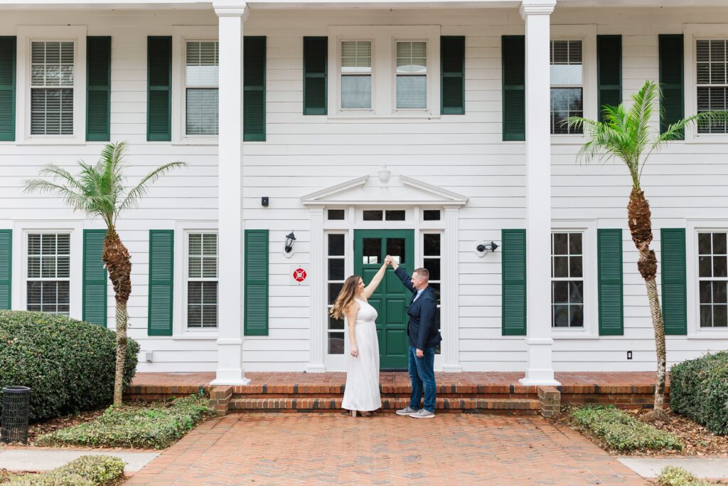 Guy twirls girl in front of Cypress Grove Estate House for their Orlando Engagement Photos at Cypress Grove Park in Orlando
