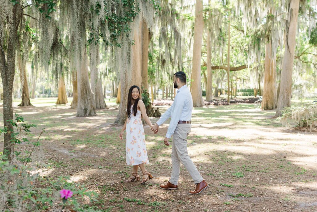 Couple walks and holds hands for their engagement photos at Kraft Azalea Garden in Winter Park, FL