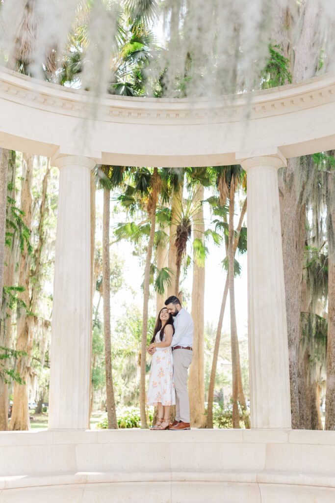 Couple snuggles together on top of the columns exedra for their engagement photos at Kraft Azalea Garden in Winter Park, FL