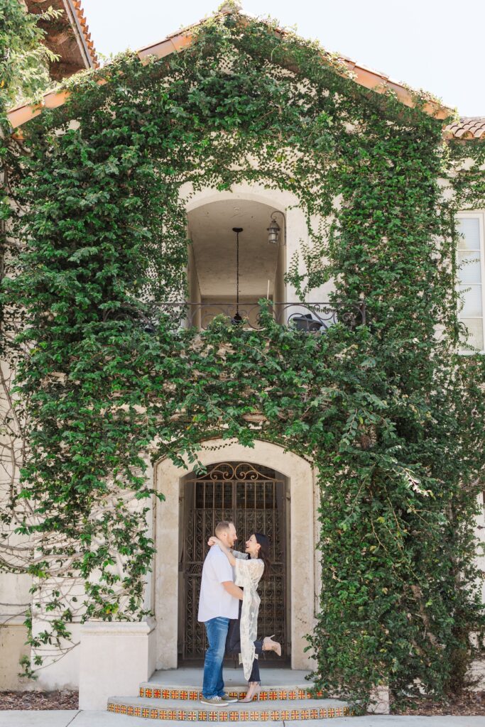 Couple wraps arms around each other and smiles in front of ivy wall at Hannibal Square in Winter Park, Florida for their engagement photos with Orlando Engagement Photographer Amy Britton Photography