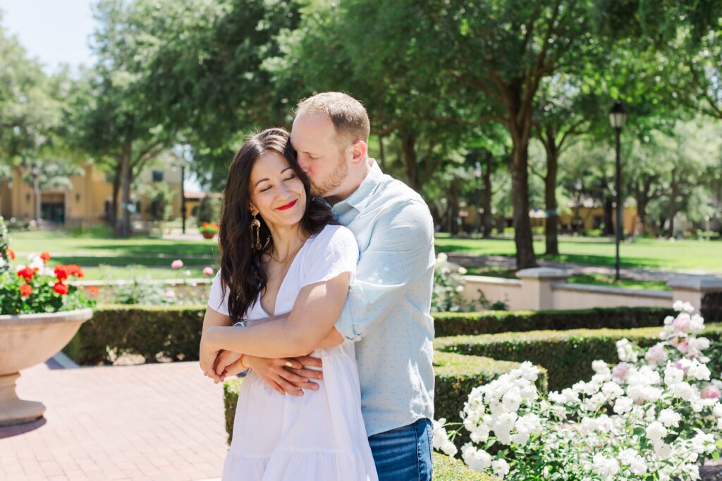 Couple wraps arms around each other in front of rose Garden at Rollins College in Winter Park, Florida for their engagement photos with Orlando Engagement Photographer Amy Britton Photography