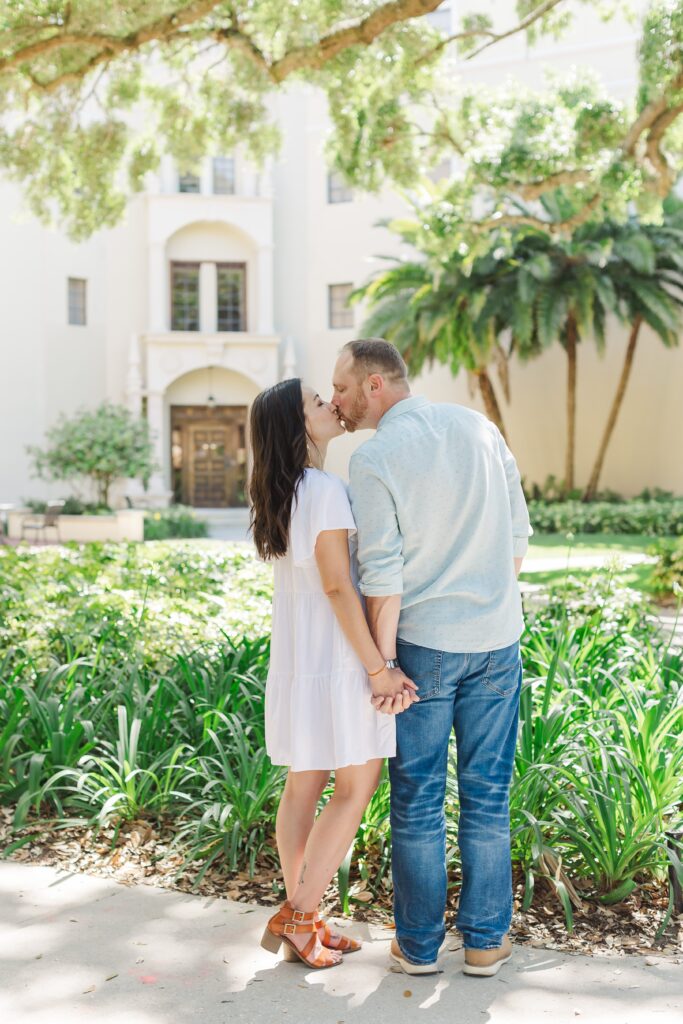 Couple kisses in front of whit building with palm trees at Rollins College in Winter Park, Florida for their engagement photos with Orlando Engagement Photographer Amy Britton Photography