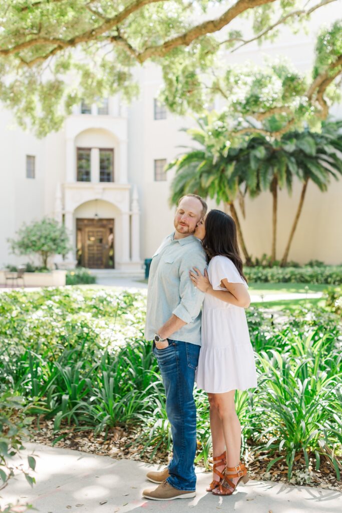 Couple kisses in front of whit building with palm trees at Rollins College in Winter Park, Florida for their engagement photos with Orlando Engagement Photographer Amy Britton Photography