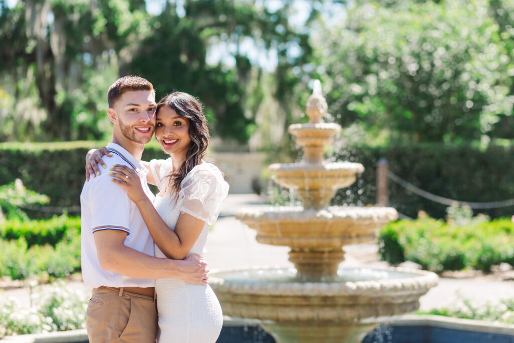Couple poses in front of fountain for their engagement photos in the rose garden at Leu Gardens in Orlando, Florida