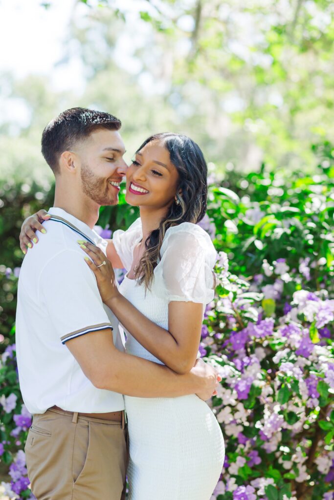 Couple laughs in front of purple flowers for their engagement photos at Leu Gardens in Orlando, Florida
