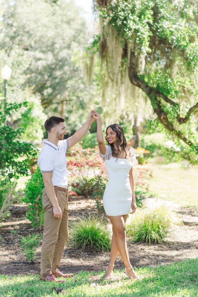 Guy twirls girl in front of large tree with hanging moss for their engagement photos at Leu Gardens in Orlando, Florida